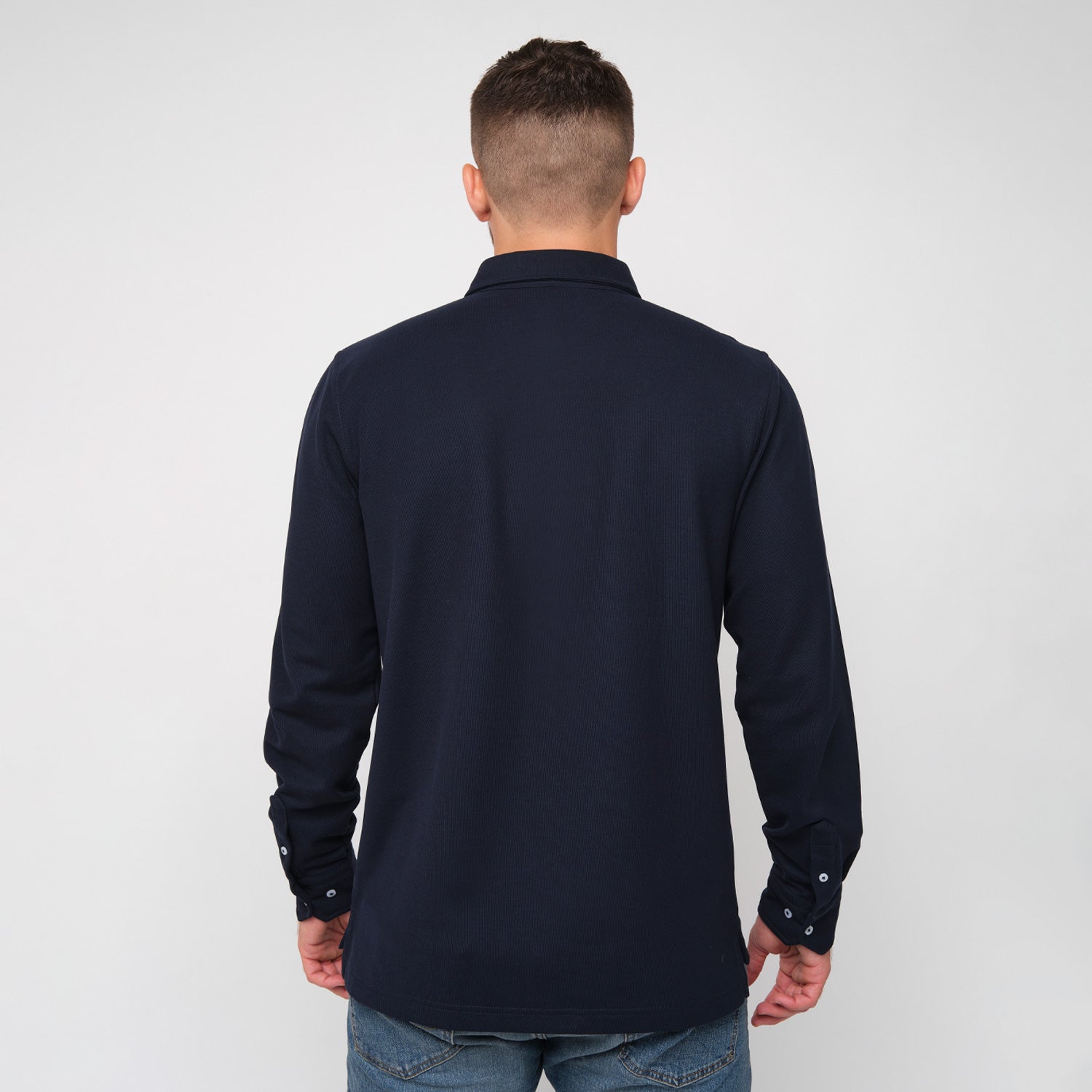 A rear view of a man wearing the navy blue button-down shirt and jeans.