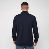 A rear view of a man wearing the navy blue button-down shirt and jeans.