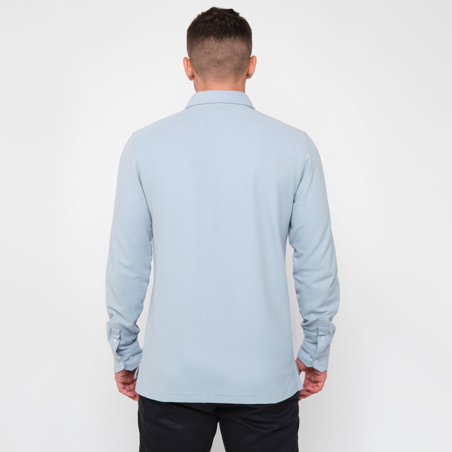 A rear view of a man wearing the light blue button-down shirt and black pants.