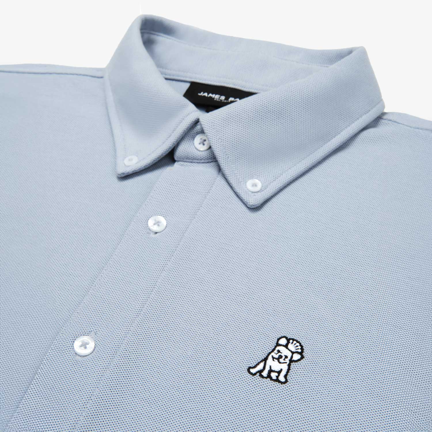 Close-up of the collar and upper part of a light blue button-down shirt, showing the buttons and embroidered logo.