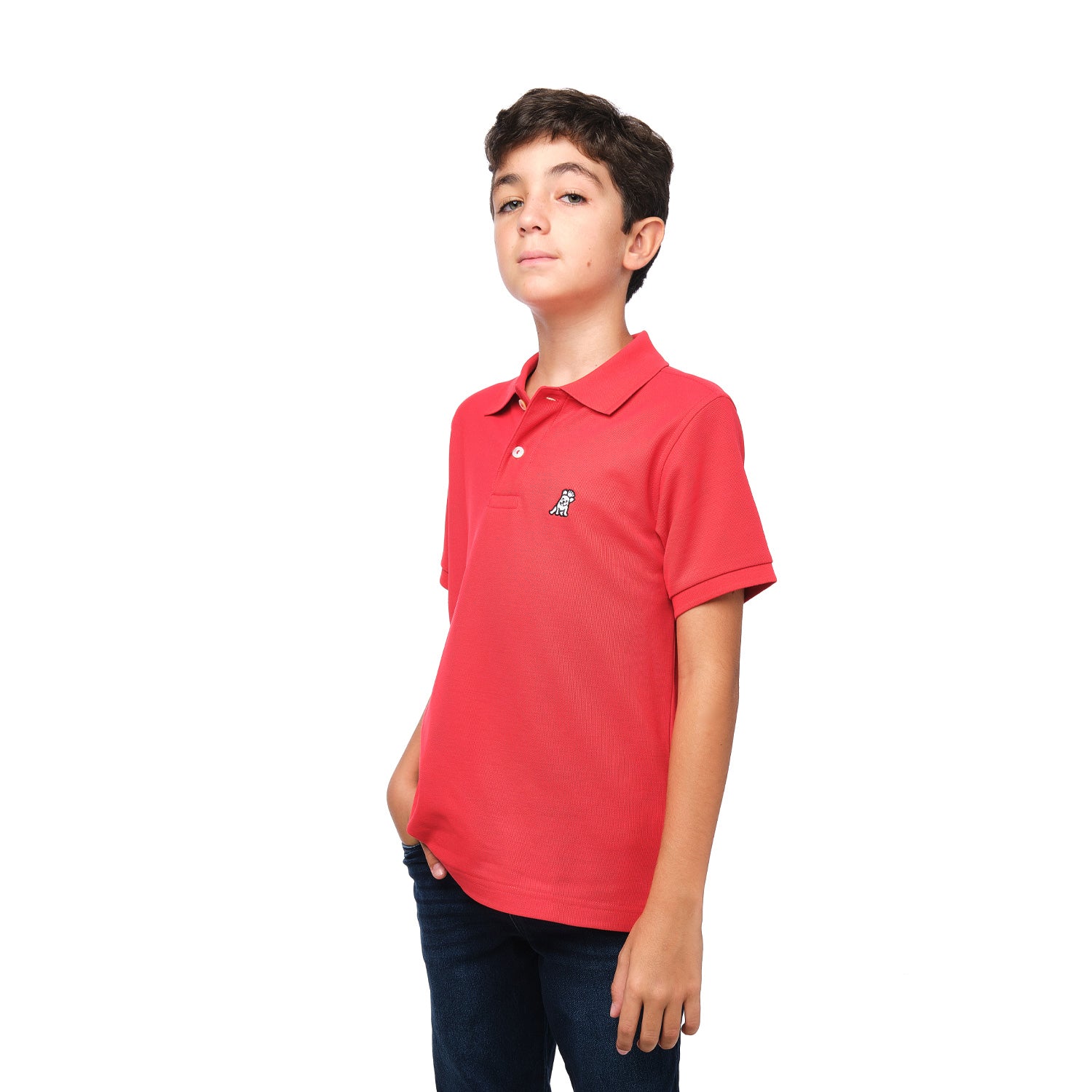 A young boy wearing a red polo shirt with a small embroidered logo on the chest, standing with his hand in his pocket and posing confidently.
