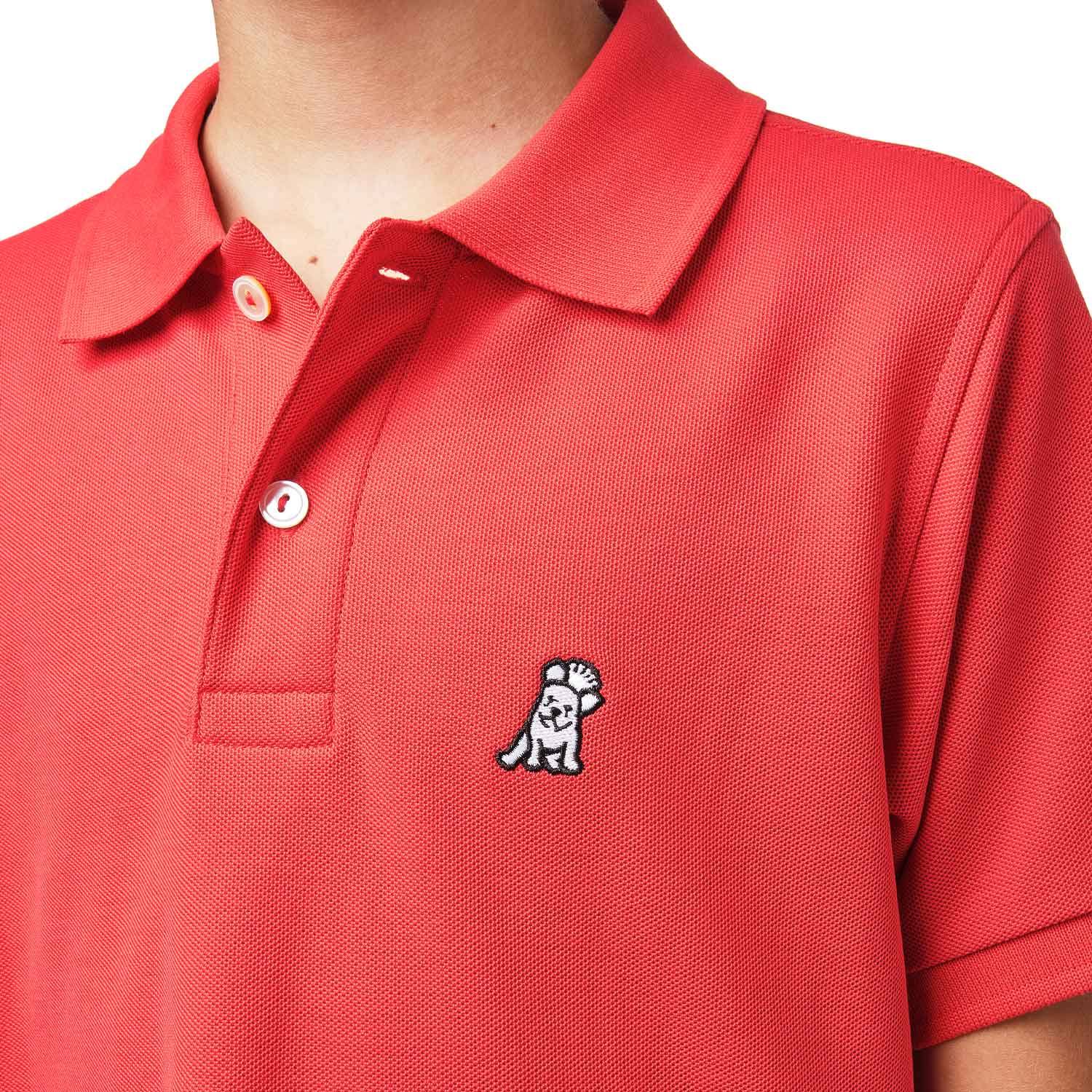 Close-up of the chest area of the red polo shirt, featuring the small embroidered logo.