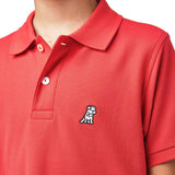 Close-up of the chest area of the red polo shirt, featuring the small embroidered logo.