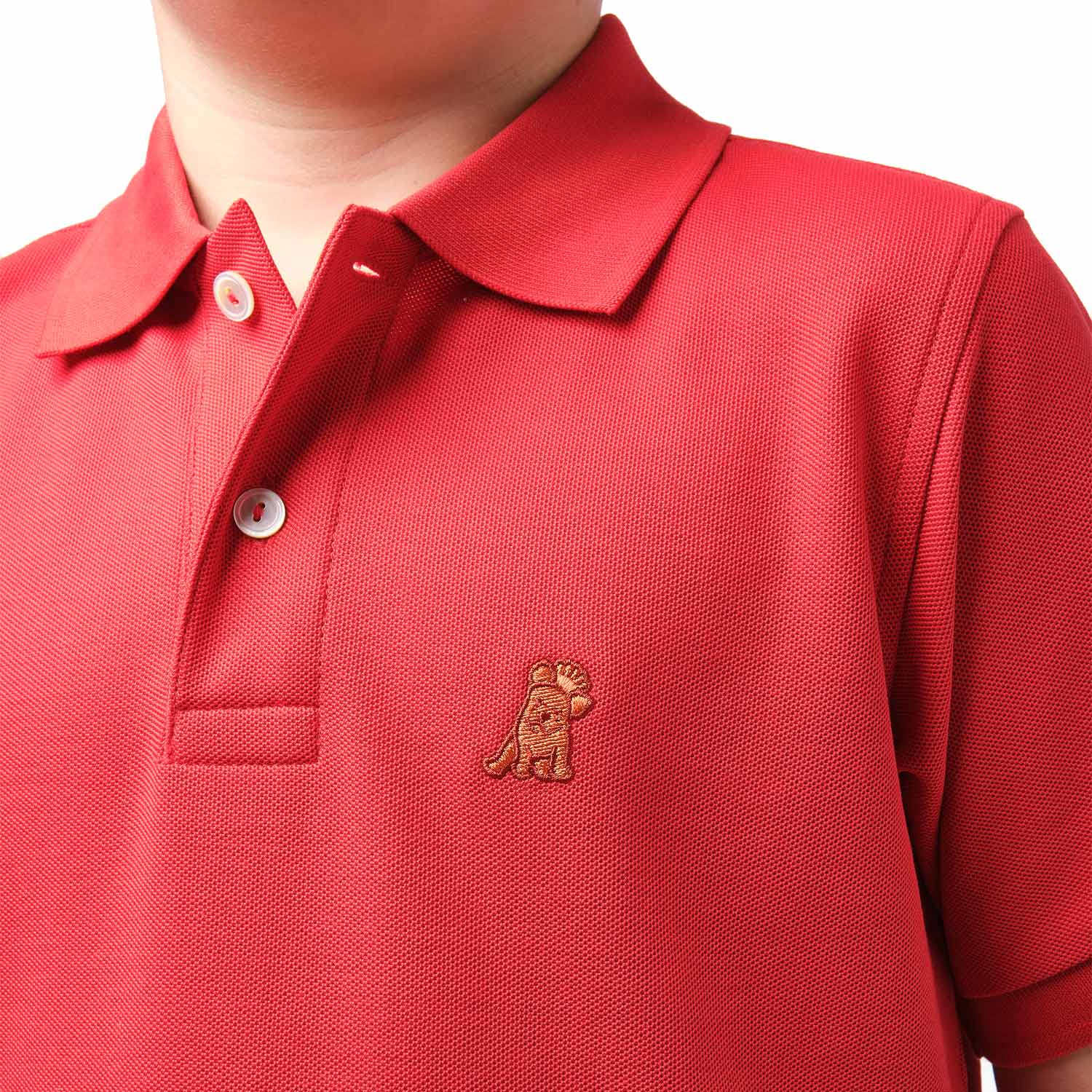 Close-up of the chest area of the red polo shirt, featuring the small gold embroidered logo.