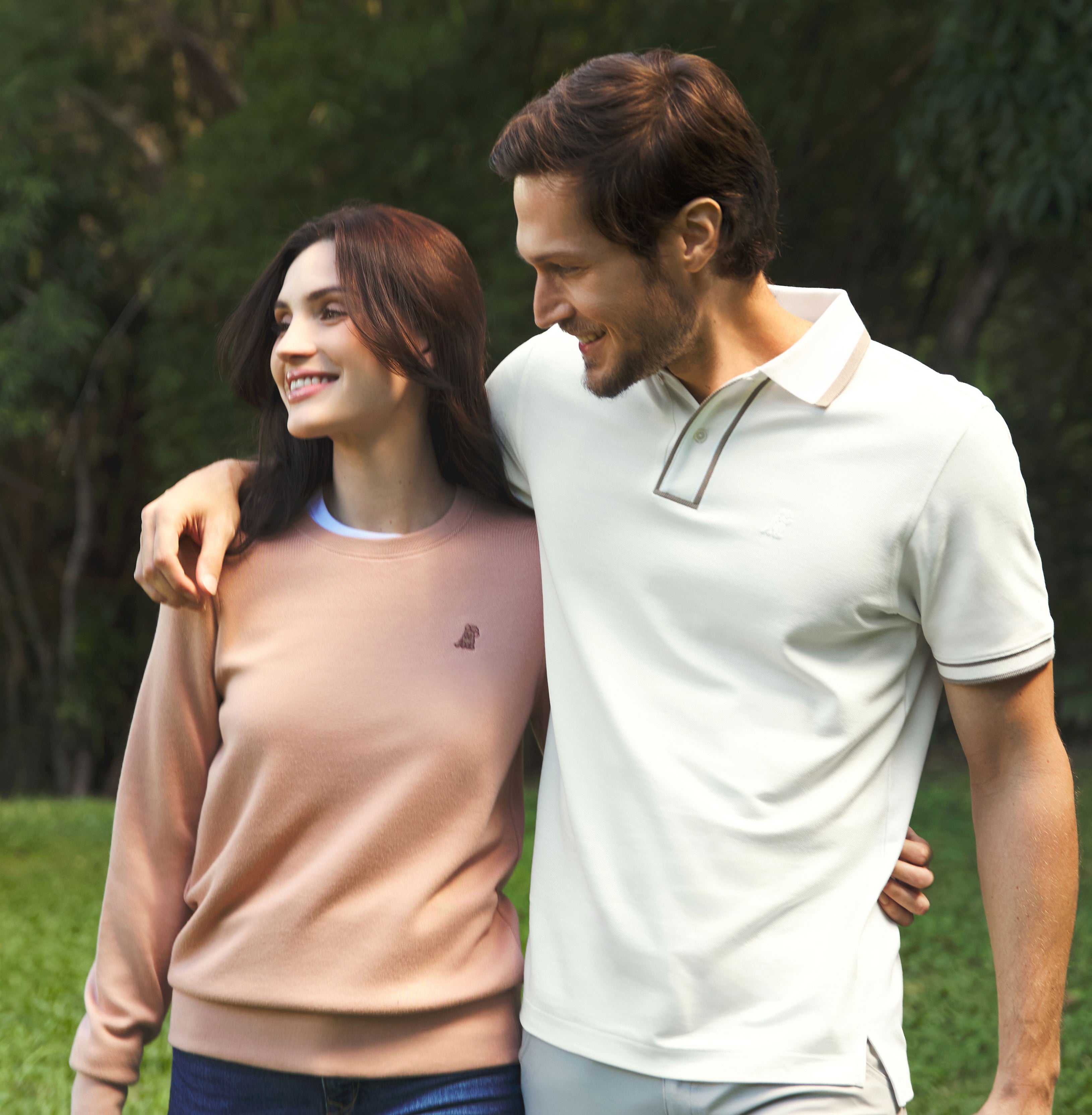 Smiling couple walking outdoors, wearing casual James Bark outfits — she in a light brown sweatshirt and he in a beige polo with contrasting trim.