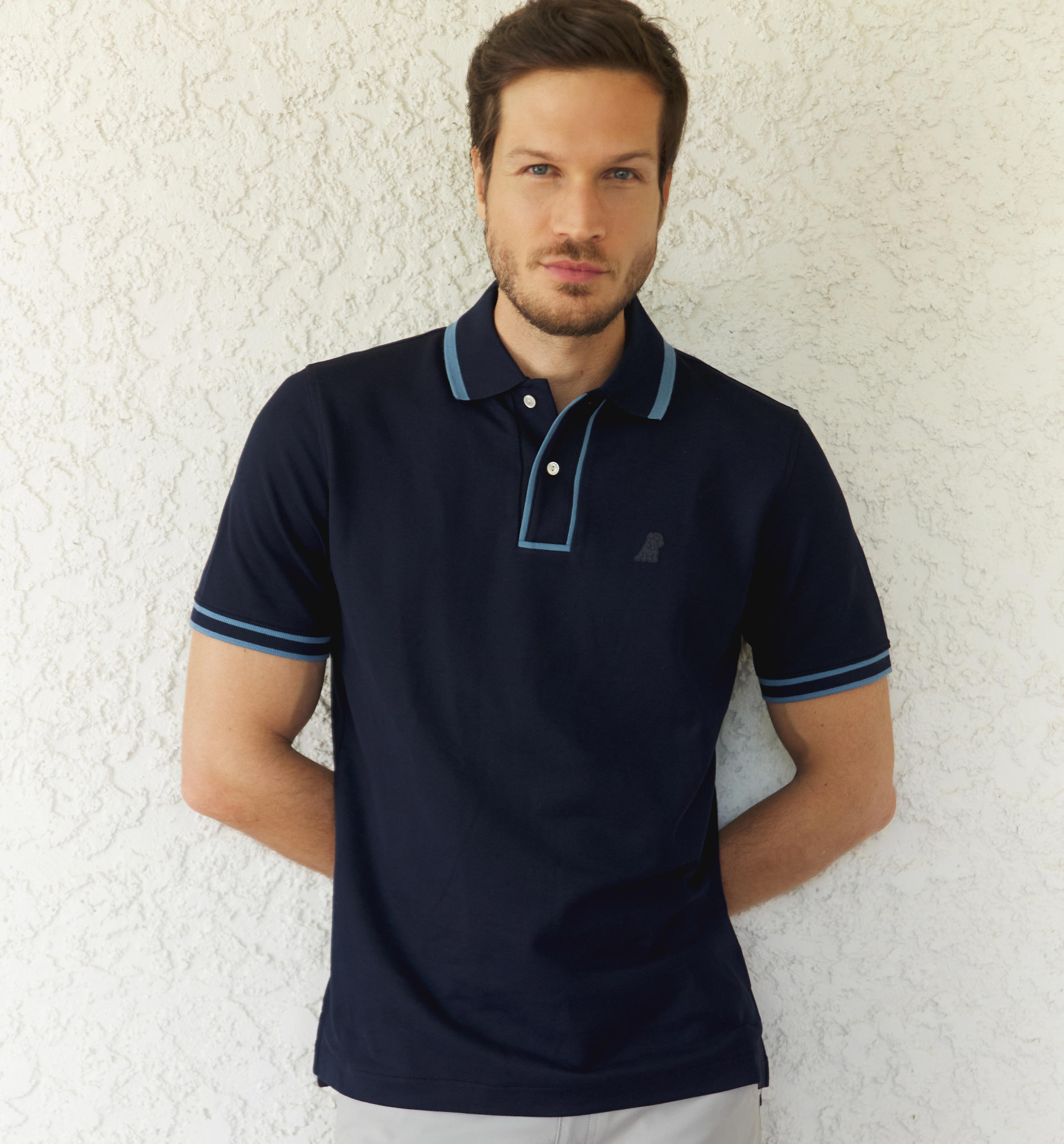 A man models a navy blue polo shirt with lighter blue trim on the collar and sleeves, and a small dark logo on the chest