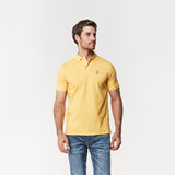 A man wearing a yellow polo shirt and jeans, standing in a casual pose, looking off to the side.