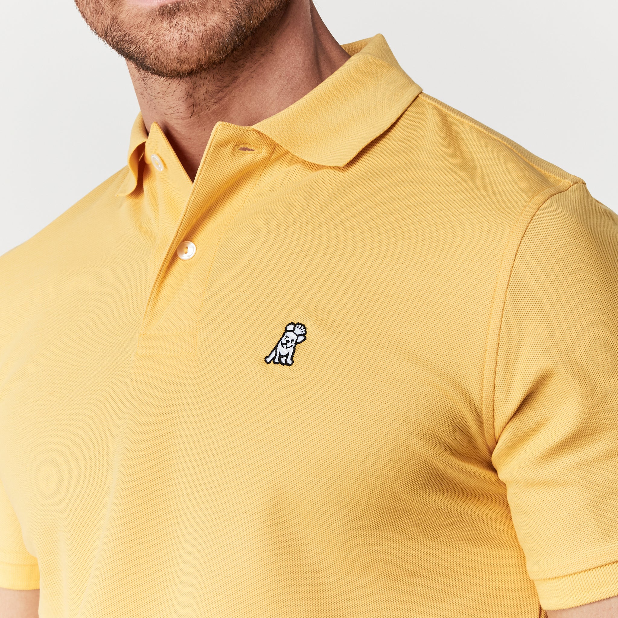 Close-up of the chest area, showing the embroidered logo on the yellow polo shirt.