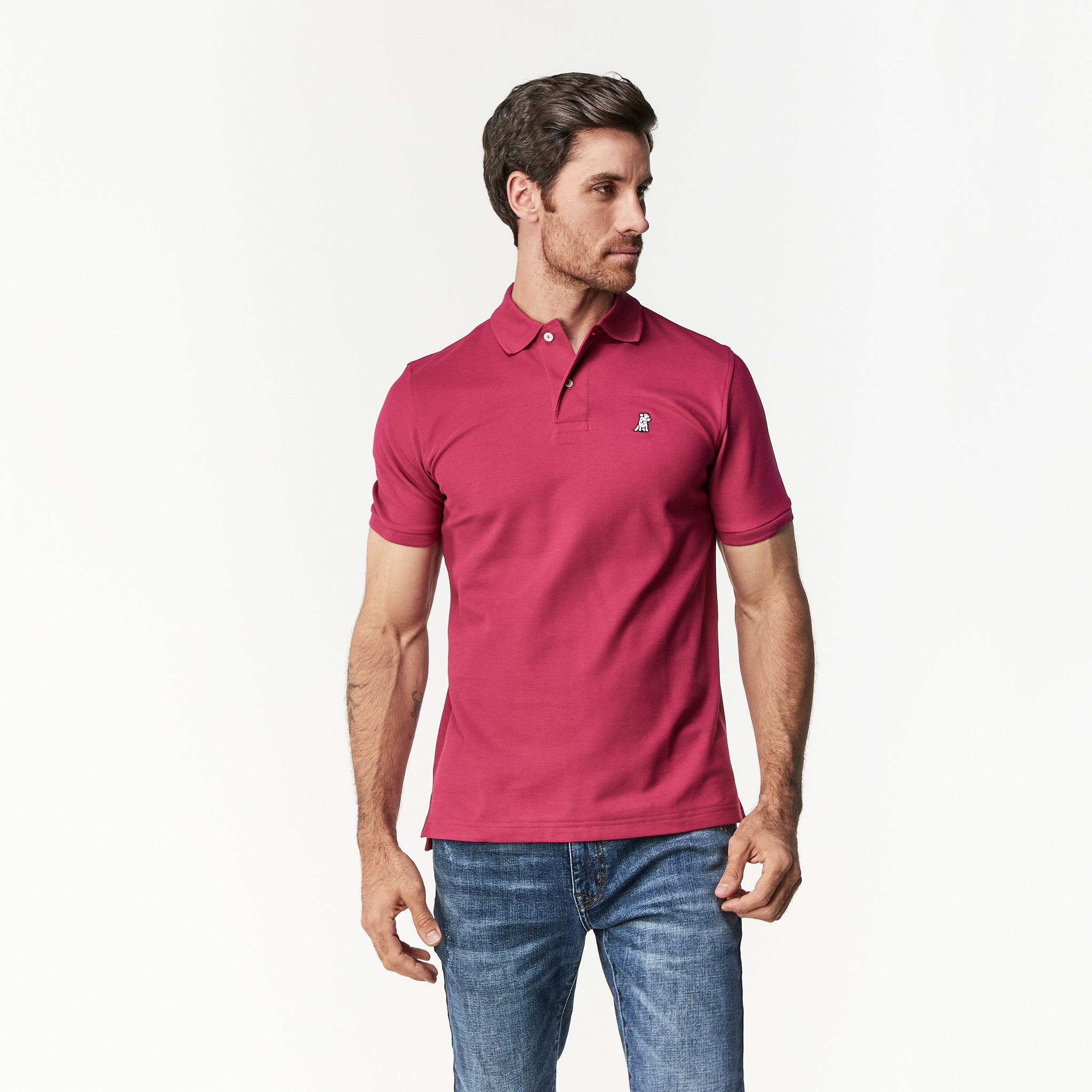 A man wearing a burgundy polo shirt and blue jeans, looking to his right in a relaxed stance.