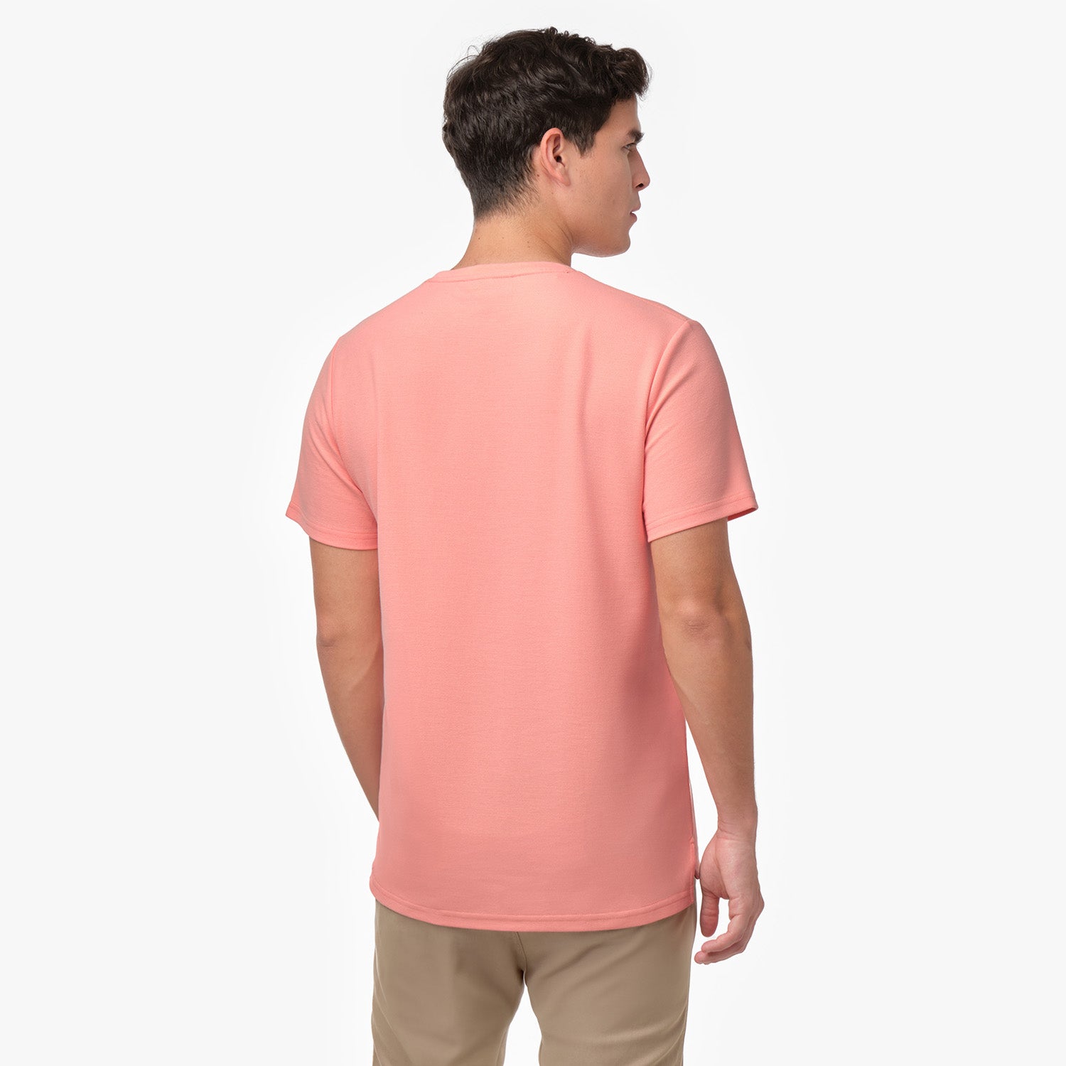 Male model showing the back of a peach/coral men's crew neck t-shirt and tan chino pants, shot on white.
