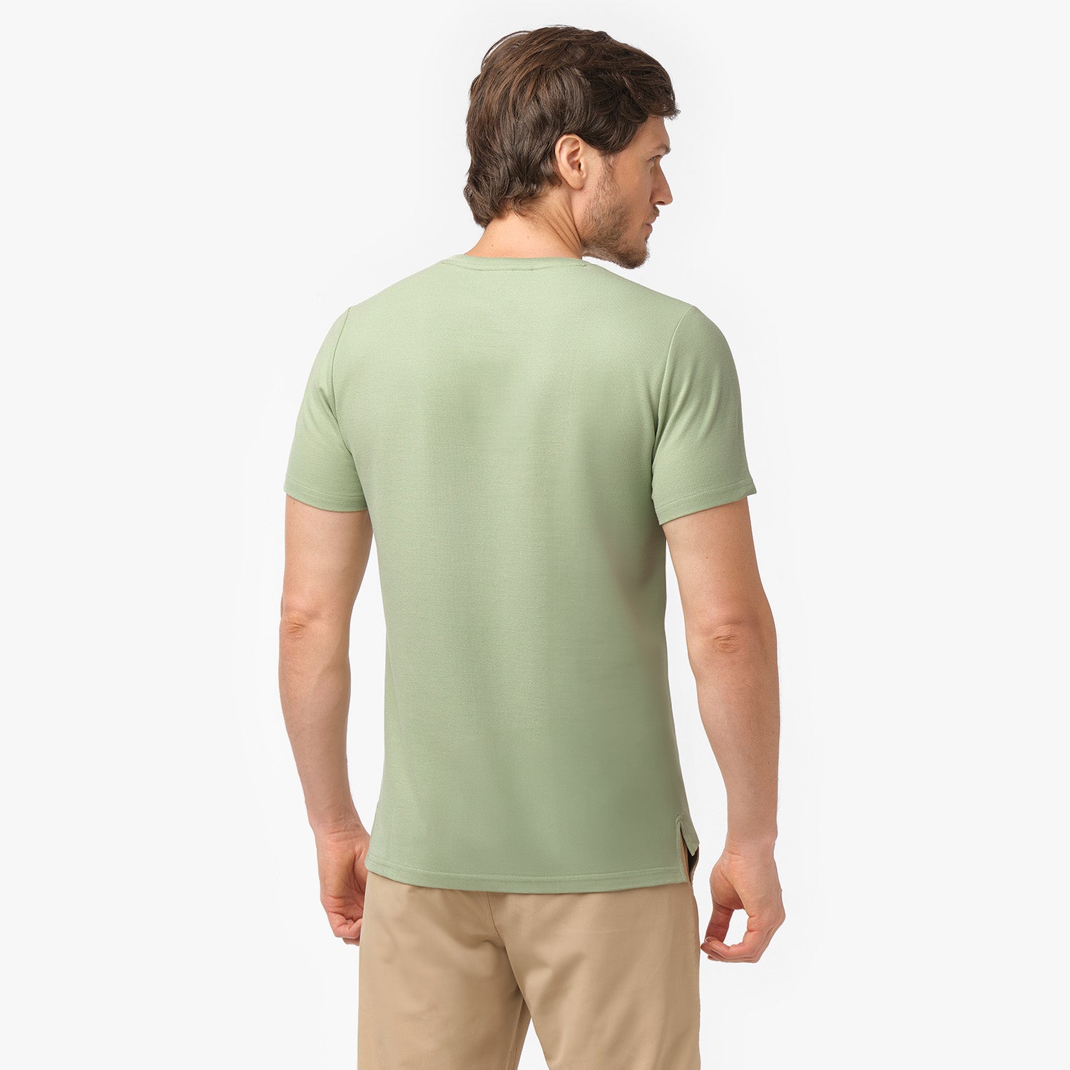 Male model showing the back of a light green men's crew neck t-shirt and tan chino pants, shot on white.