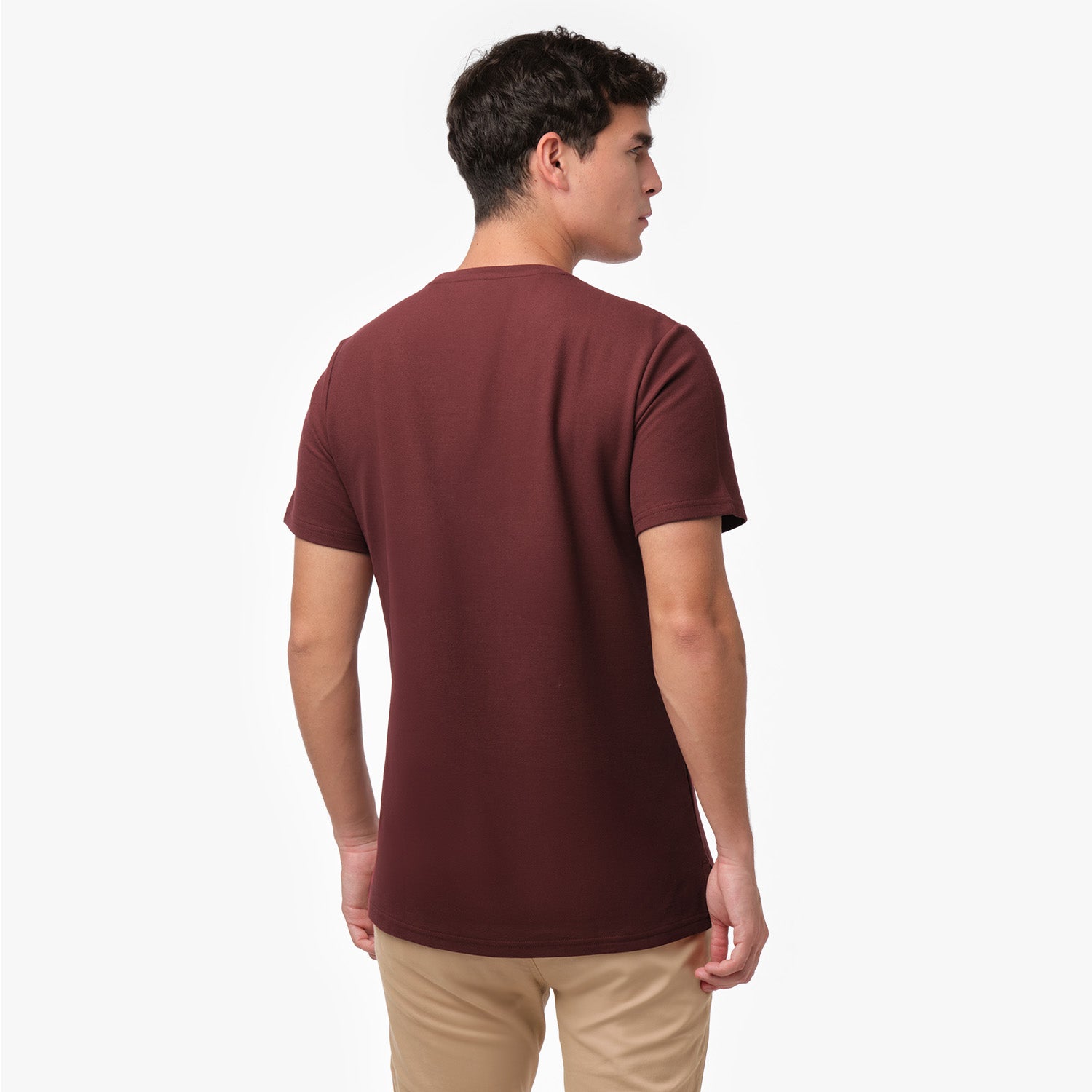 Male model showing the back of a maroon men's crew neck t-shirt and tan chino pants, shot on white.