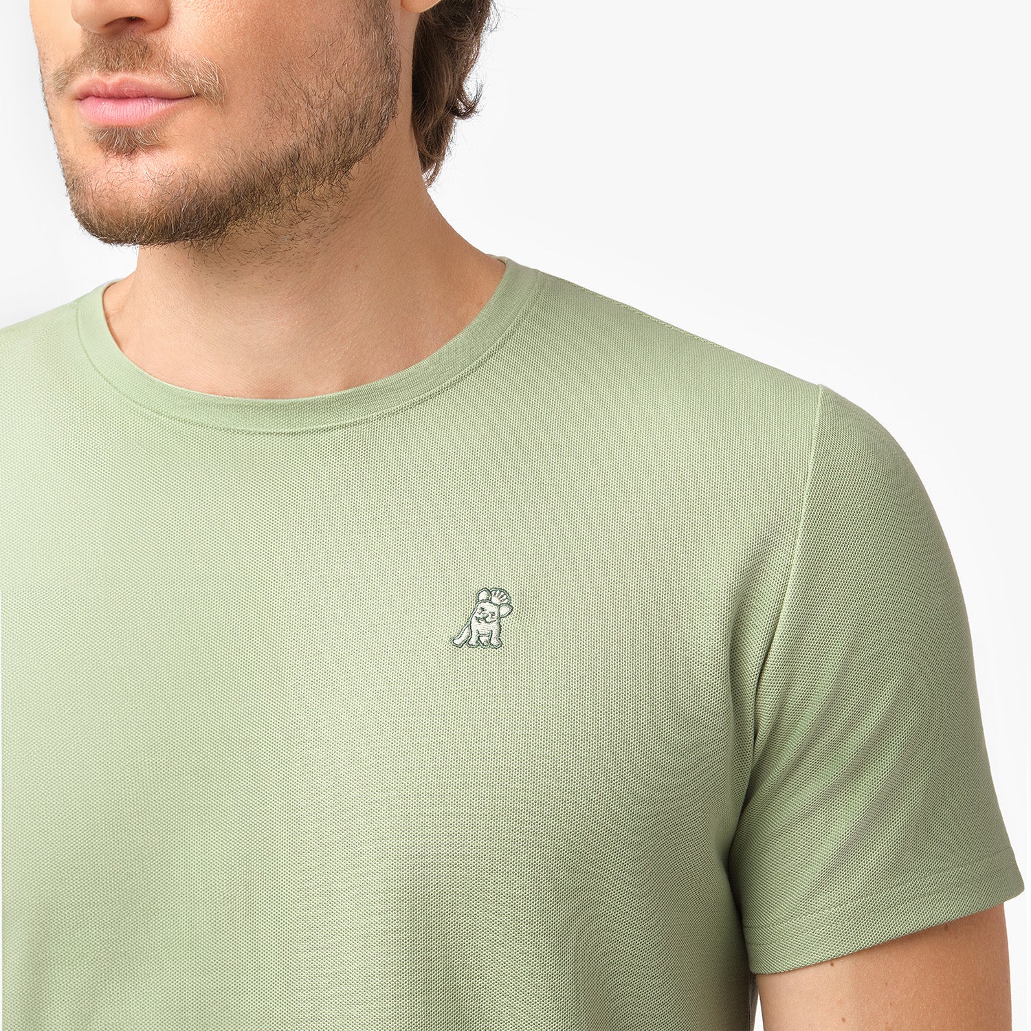 Detailed view of the embroidered logo on the left chest of a light green textured t-shirt.