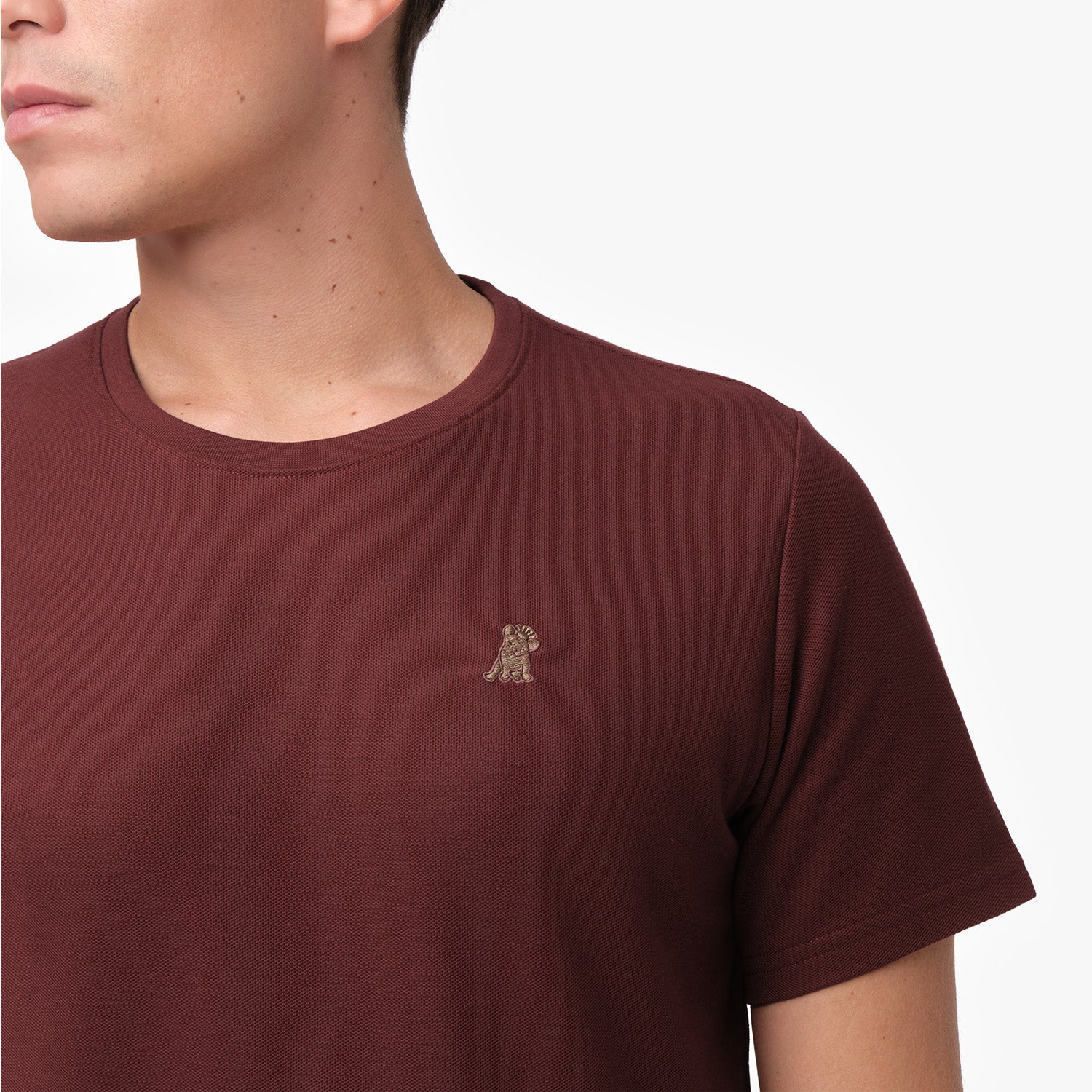 Detailed view of the embroidered logo on the left chest of a maroon textured t-shirt.