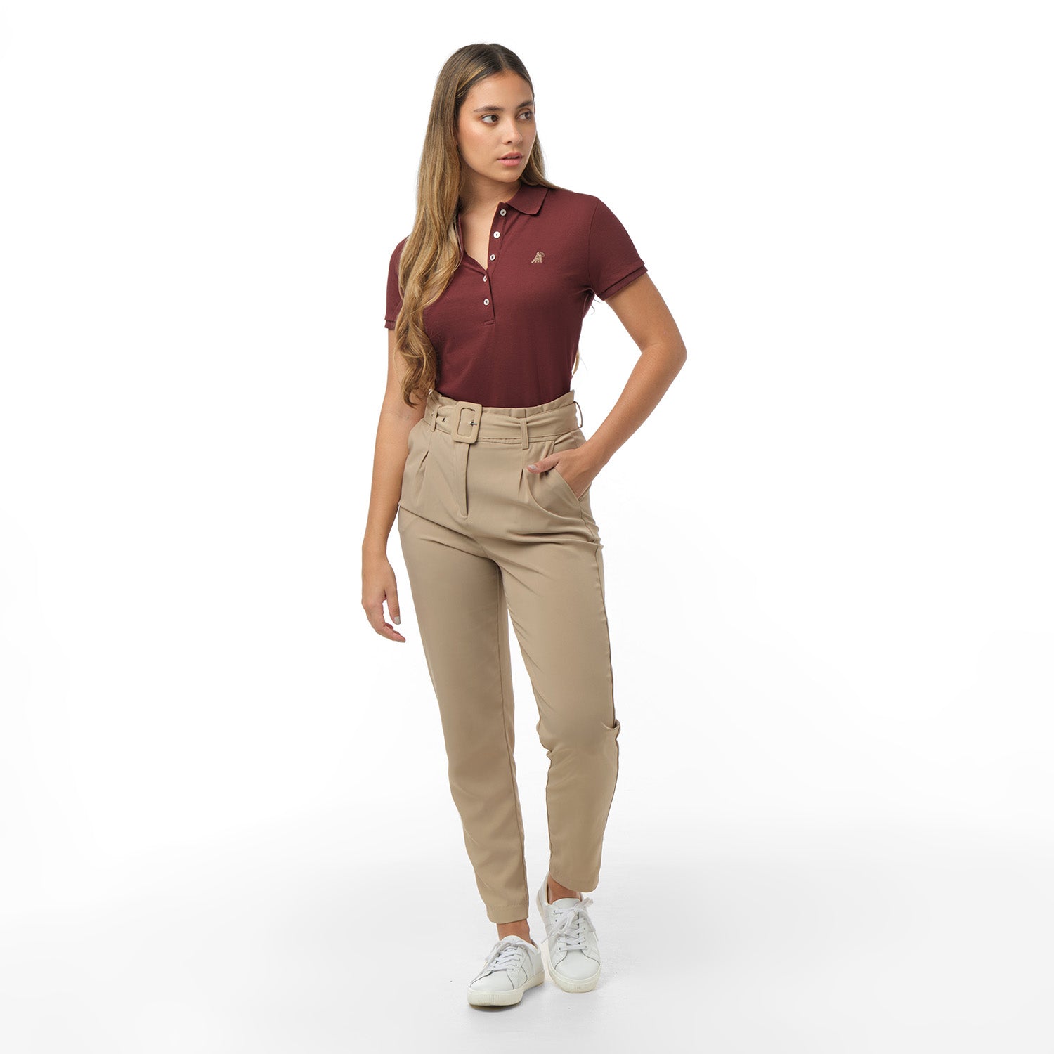 Full-length view of a woman modeling a maroon short-sleeve polo shirt, high-waisted beige trousers with a belt, and white sneakers. Standing pose against white background
