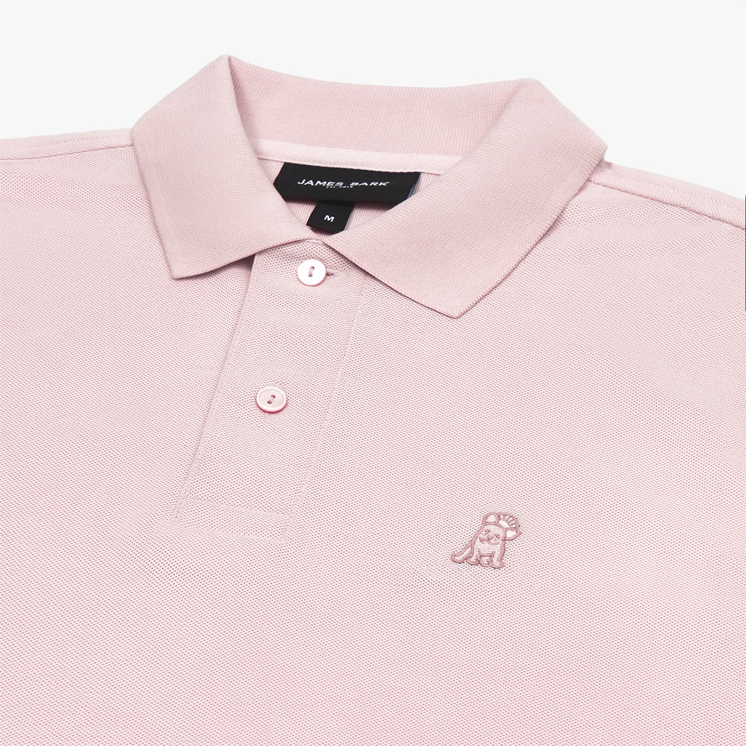 Detailed close-up of the light pink embroidered dog logo on a pink polo shirt