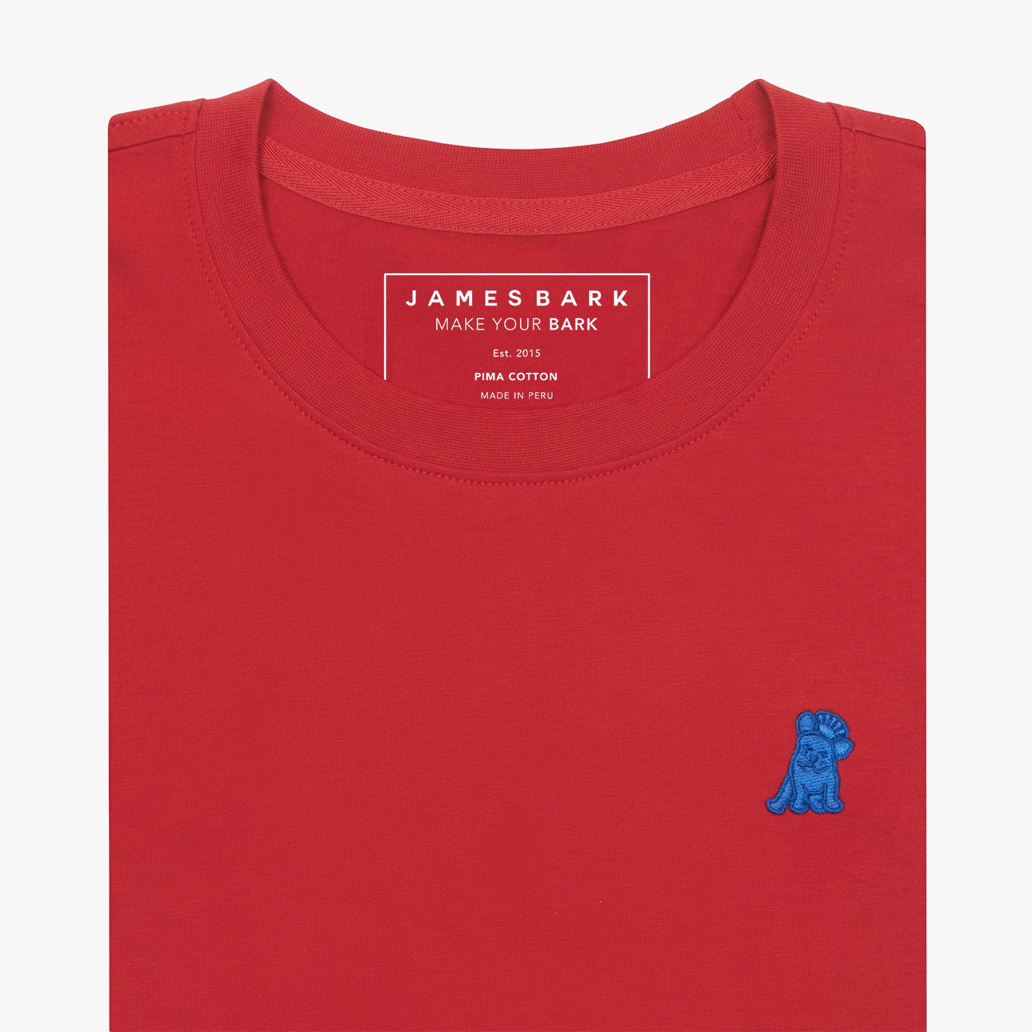 Close-up of the neckline area of a red t-shirt, showing the James Bark brand tag, Pima Cotton detail, and a blue embroidered dog logo