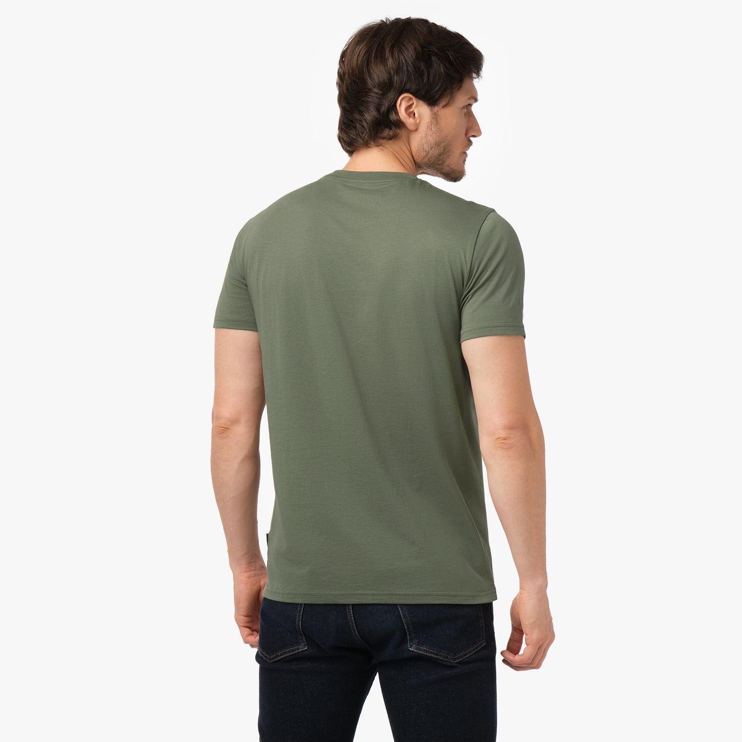 Back view of the male model wearing the solid olive green crew neck t-shirt and dark blue jeans, looking over his left shoulder