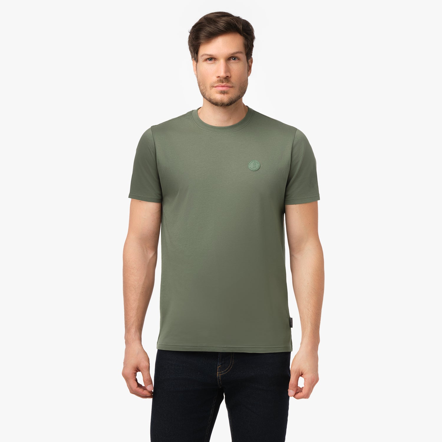 Male model facing forward wearing the solid olive green crew neck t-shirt featuring a tonal embossed circular logo on the left chest, paired with dark blue jeans