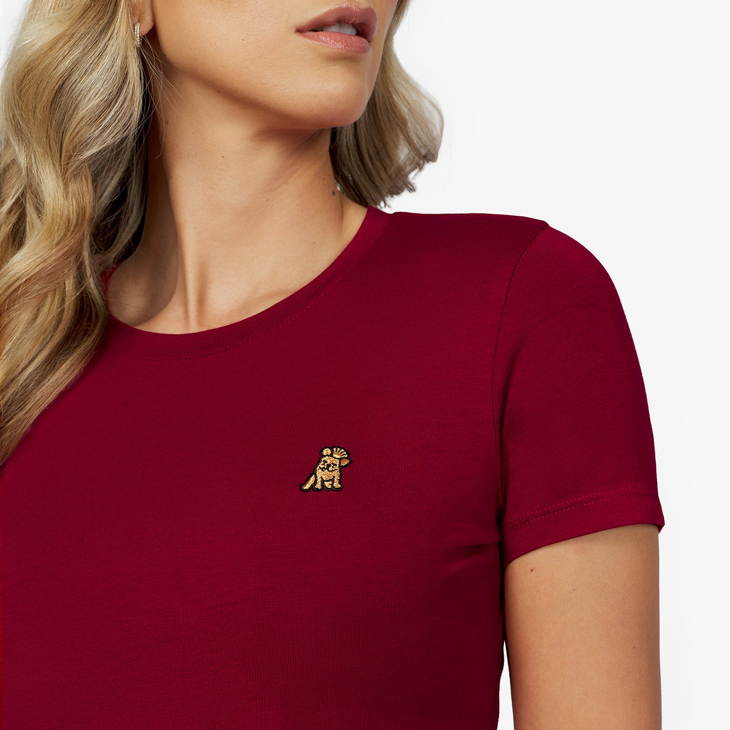 Close-up detail of the burgundy crew neck t-shirt, showing the fabric texture and the small gold embroidered dog logo on the left chest