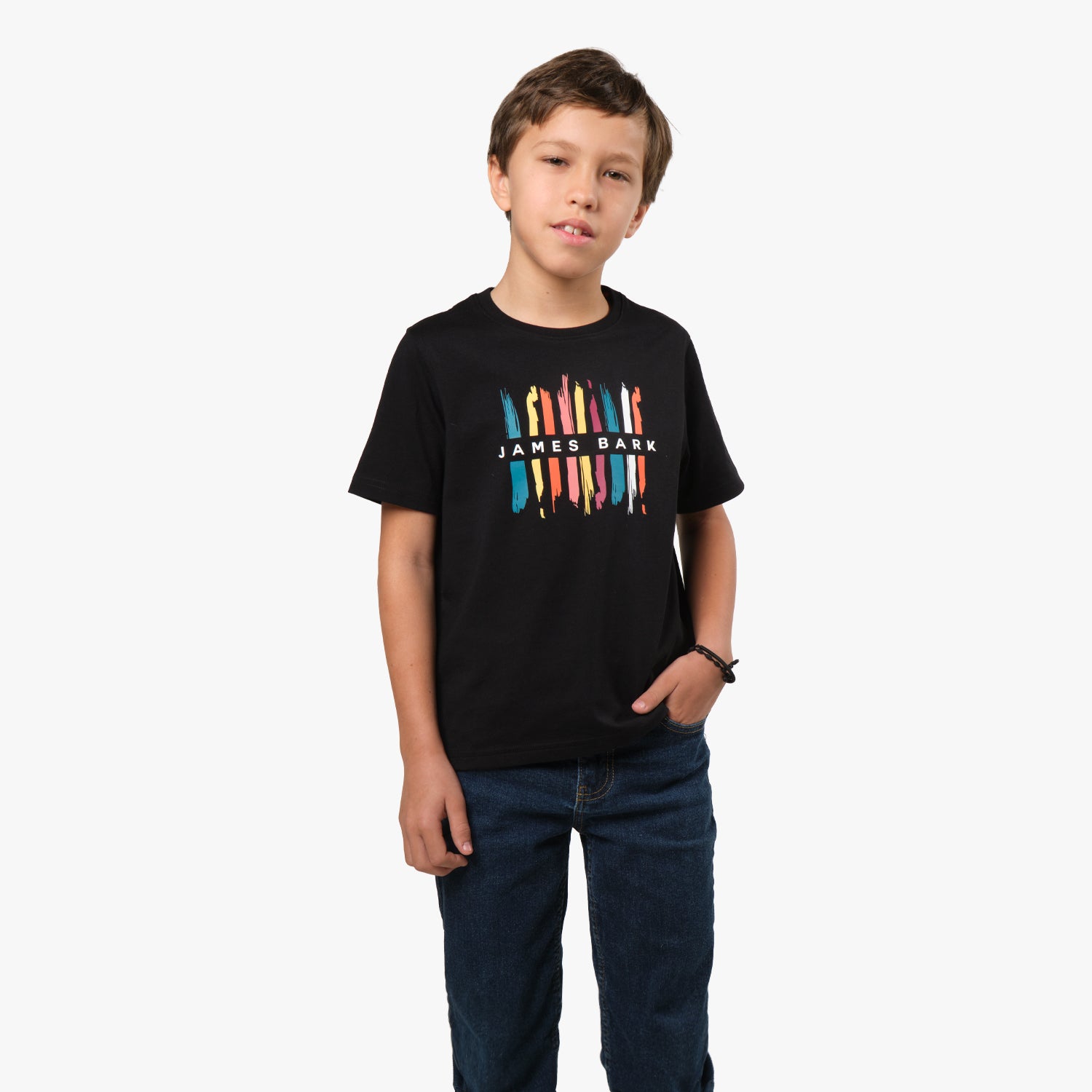 A young boy wearing a black T-shirt with a colorful graphic design on the front, showing multiple colored pencils arranged vertically. He is standing with his hands at his sides, looking forward.