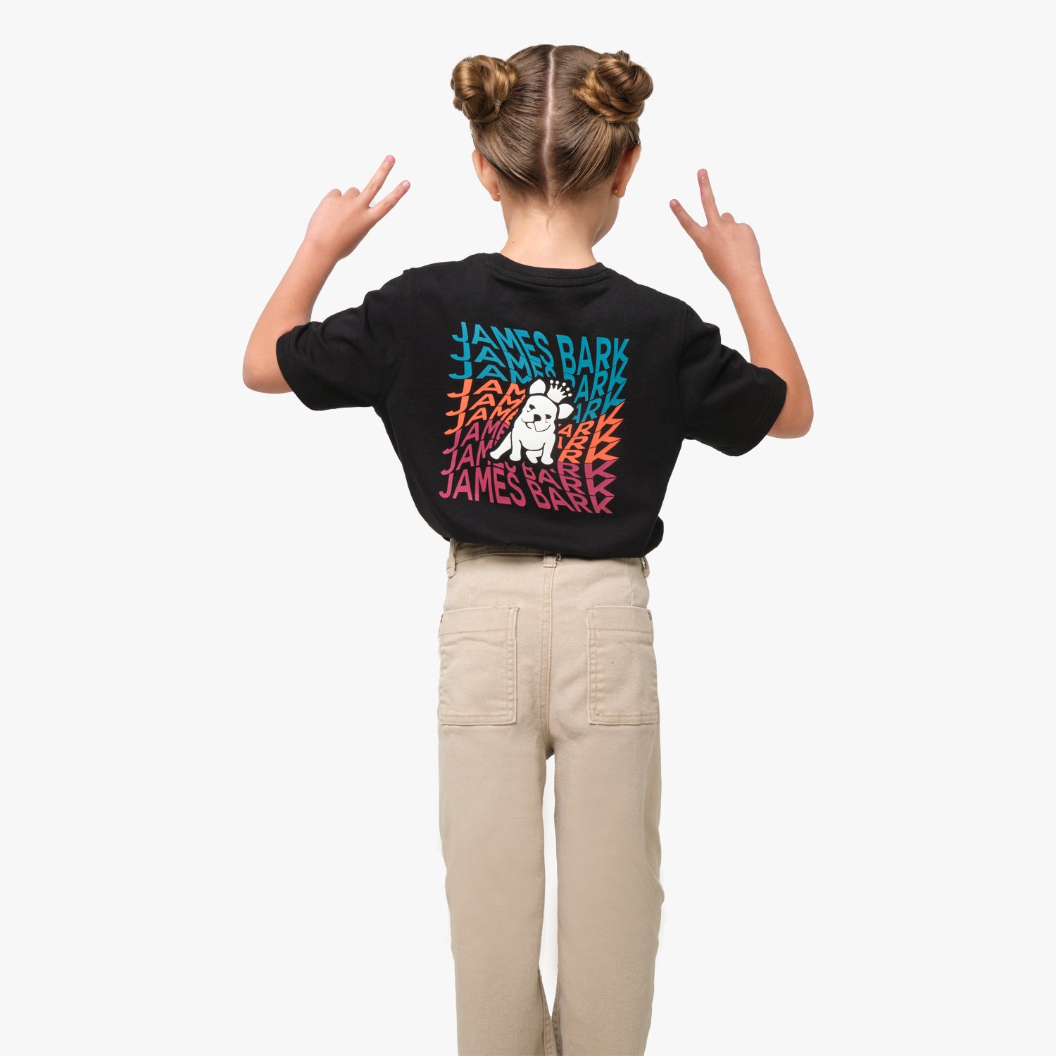 Rear view of a girl wearing a black t-shirt with colorful "JAMES BARK" text radiating outward from a cartoon dog graphic, with her hands raised showing peace signs.