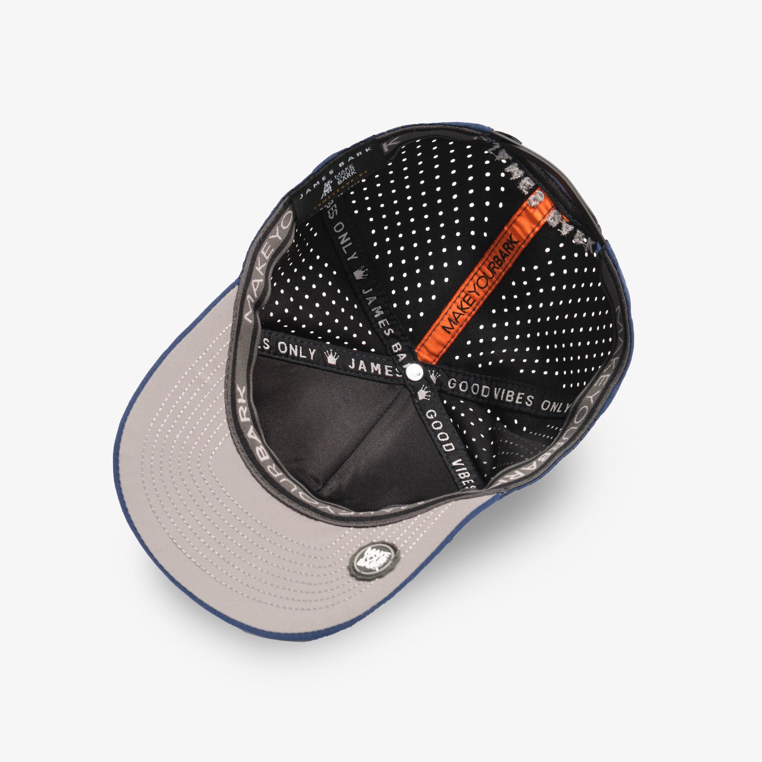 A top-down view of a baseball cap with a light gray brim, black dotted interior panels, and an orange accent strap with white text