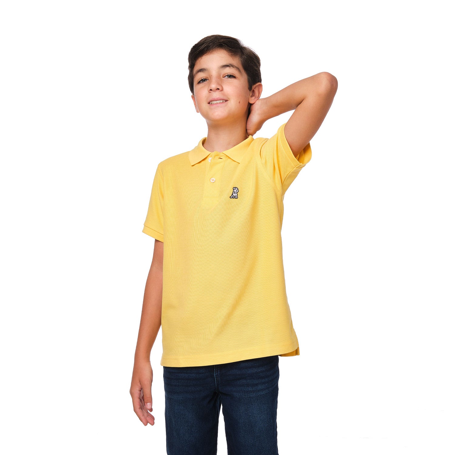 A young boy wearing a yellow polo shirt with a small embroidered logo on the chest, standing with one arm raised behind his head and smiling.