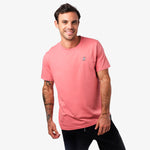 Front view of a man wearing a pink t-shirt: The man is standing casually, smiling while wearing a pink t-shirt with a small embroidered dog logo on the left chest.