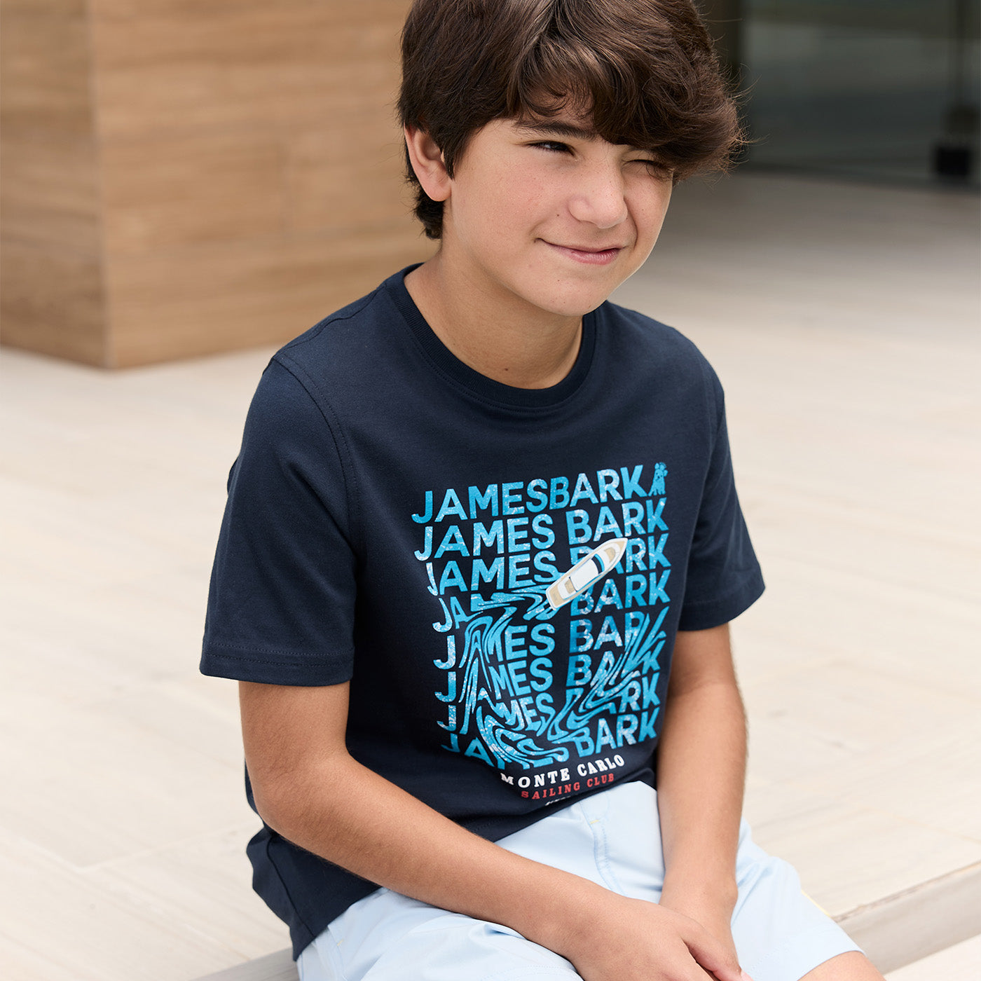 Boy wearing a navy blue James Bark graphic t-shirt featuring a boat design and text print.