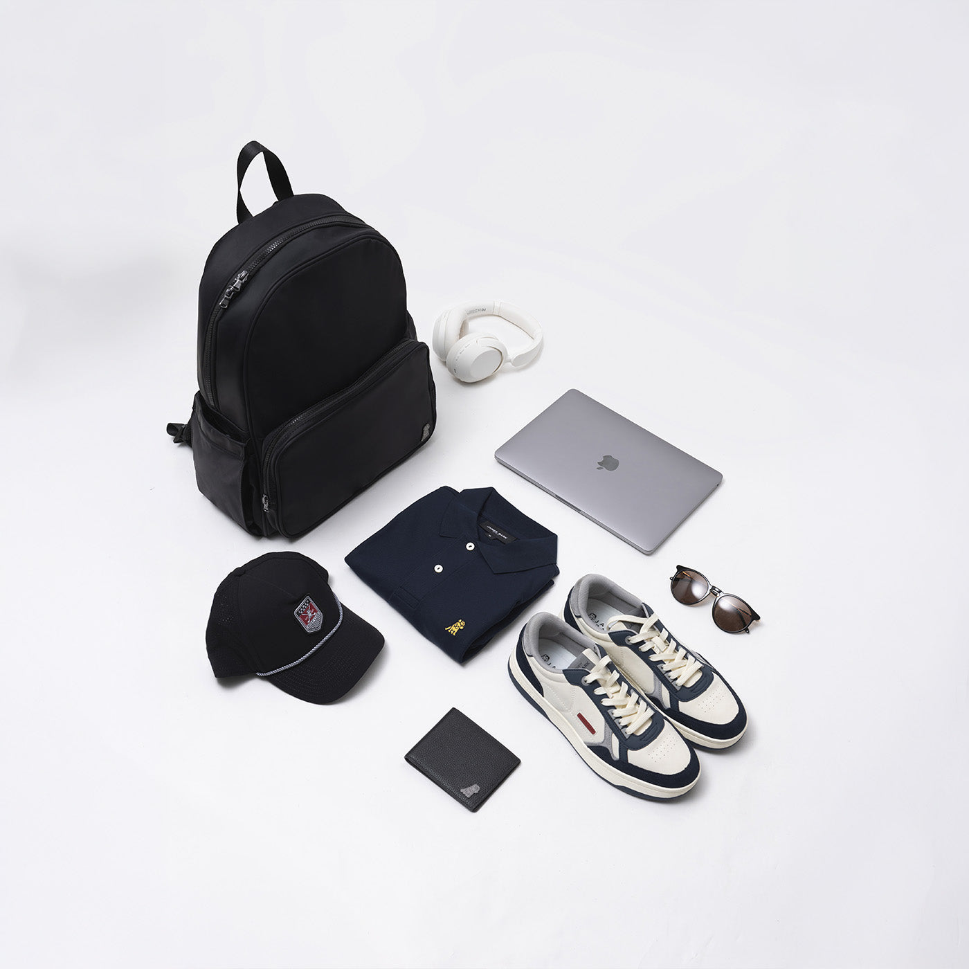 James Bark backpack, laptop, headphones, polo shirt, cap, wallet, sunglasses, and sneakers laid out on a white surface.