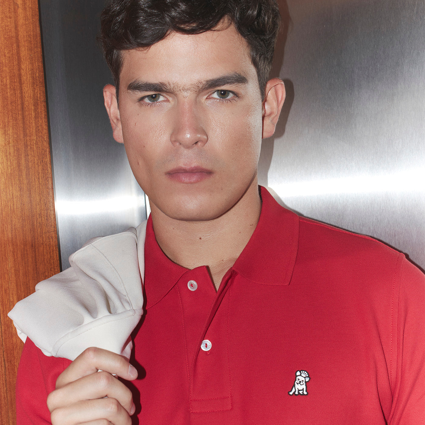 Man wearing a red polo shirt with a logo, holding a white jacket.