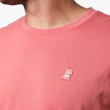 Close-up of the upper chest area of the salmon pink t-shirt, focusing on the small embroidered animal logo near the neckline.