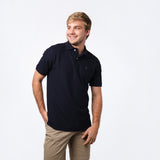 A young man smiling, wearing a navy blue polo shirt with an embroidered logo on the chest, paired with beige trousers.