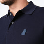 Close-up of the embroidered logo on the chest of the navy blue polo shirt.
