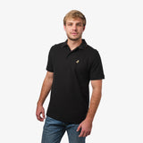 Front view of a man wearing a black polo shirt: The polo features a subtle gold embroidered dog logo on the left chest, and the man is casually standing with one hand by his side.