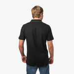 Back view of a man wearing the black polo shirt: The man is standing, showing the simple and clean design of the back of the polo shirt.