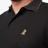 Close-up of the embroidered logo on the black polo shirt: A gold embroidered dog logo is visible on the left chest area, adding a subtle detail to the polo.