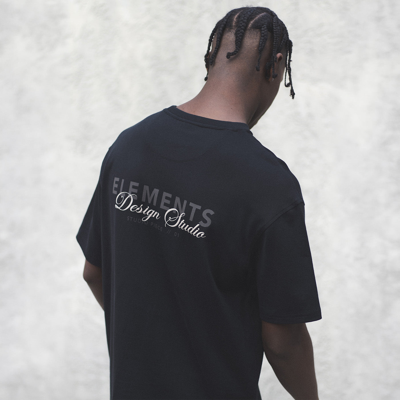 Man wearing a black James Bark 'Elements Design Studio' graphic t-shirt, viewed from behind.