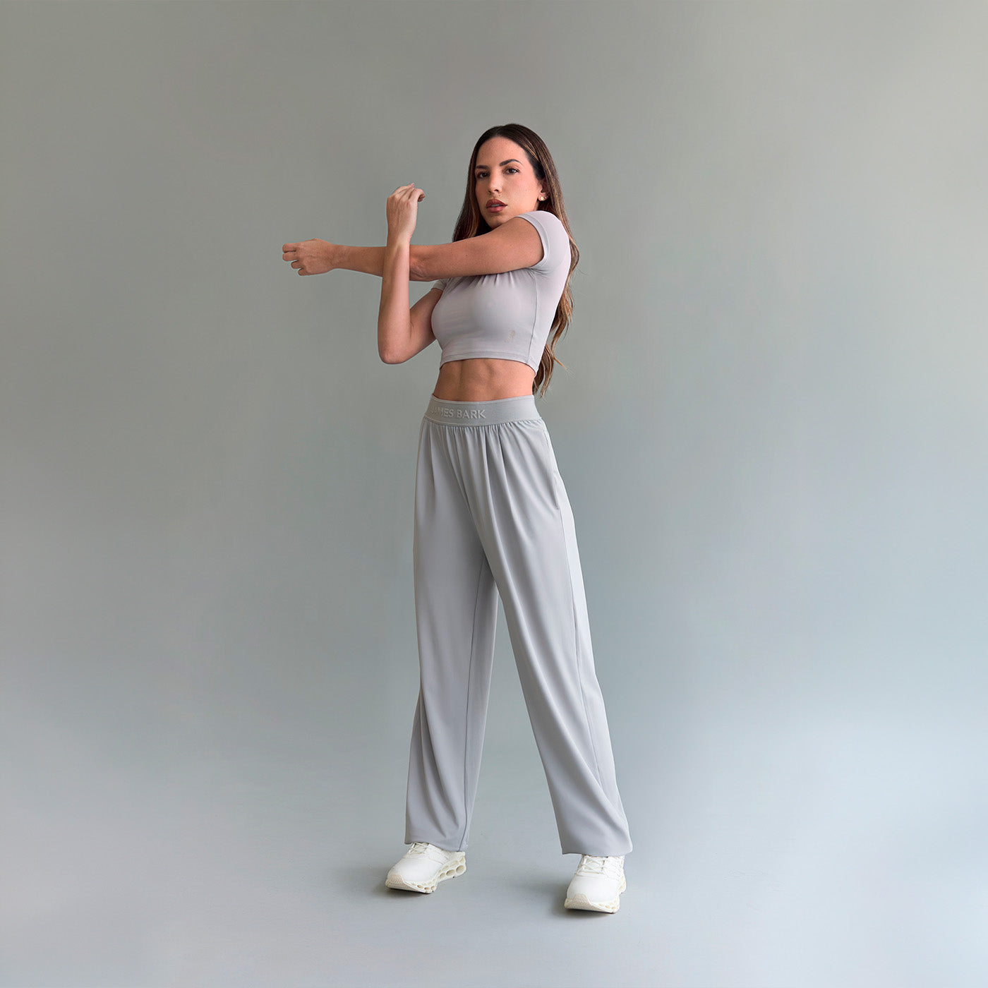 Woman in gray athletic wear stretching against a plain background