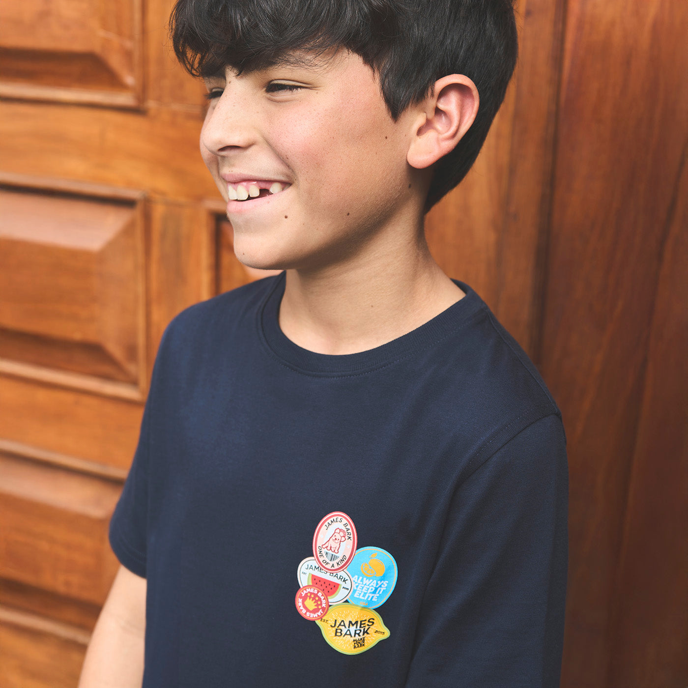 Young boy wearing a navy blue t-shirt with colorful patches against a wooden background