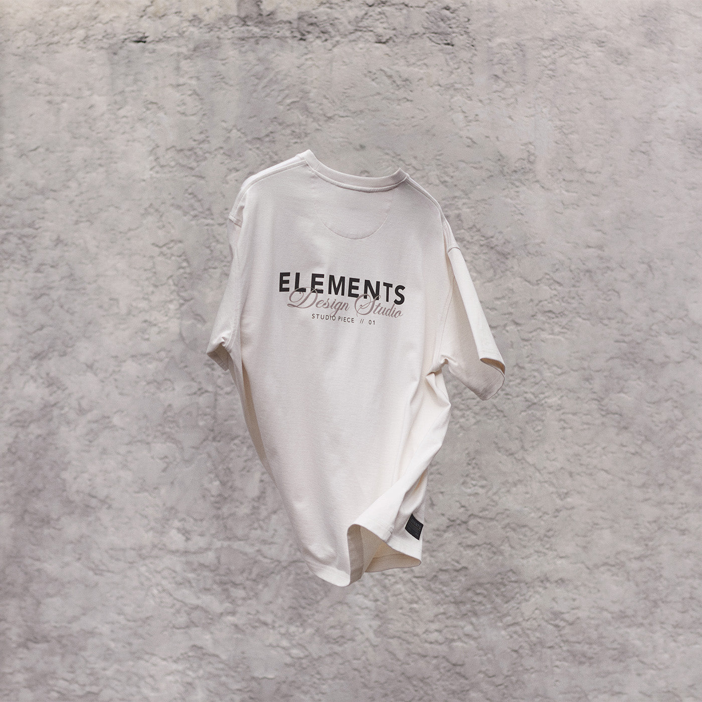 White t-shirt with 'ELEMENTS' text on a textured gray background