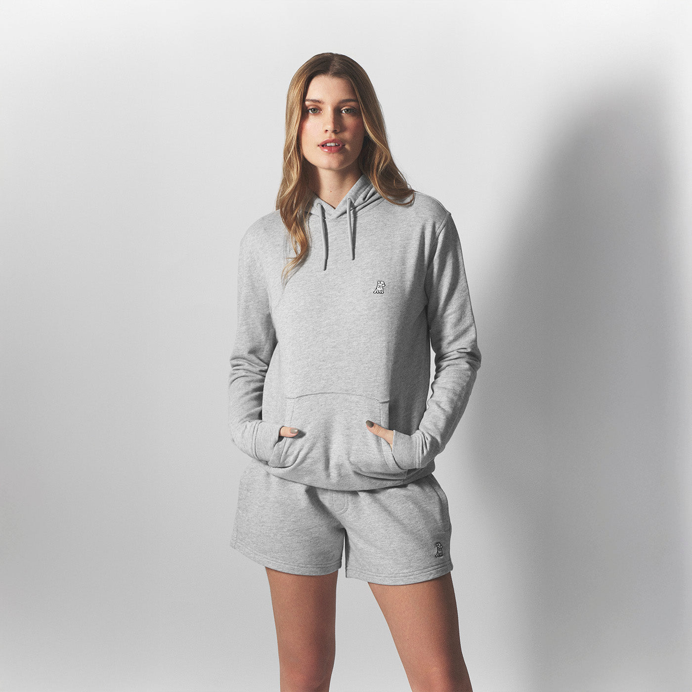 Woman wearing a gray hoodie and shorts set on a plain background
