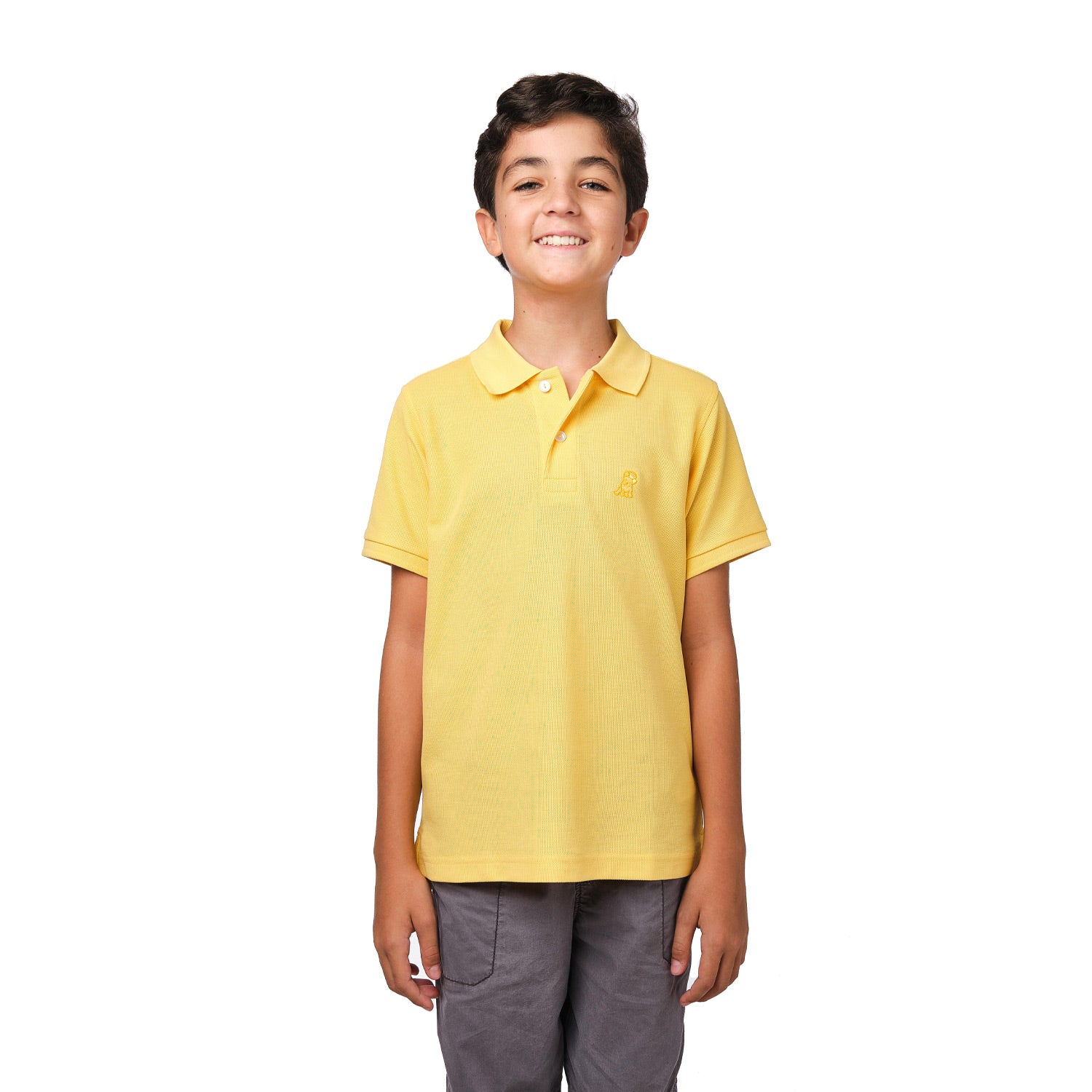 A young boy wearing a yellow polo shirt with a small gold embroidered logo on the chest, standing and smiling with his hands at his sides.