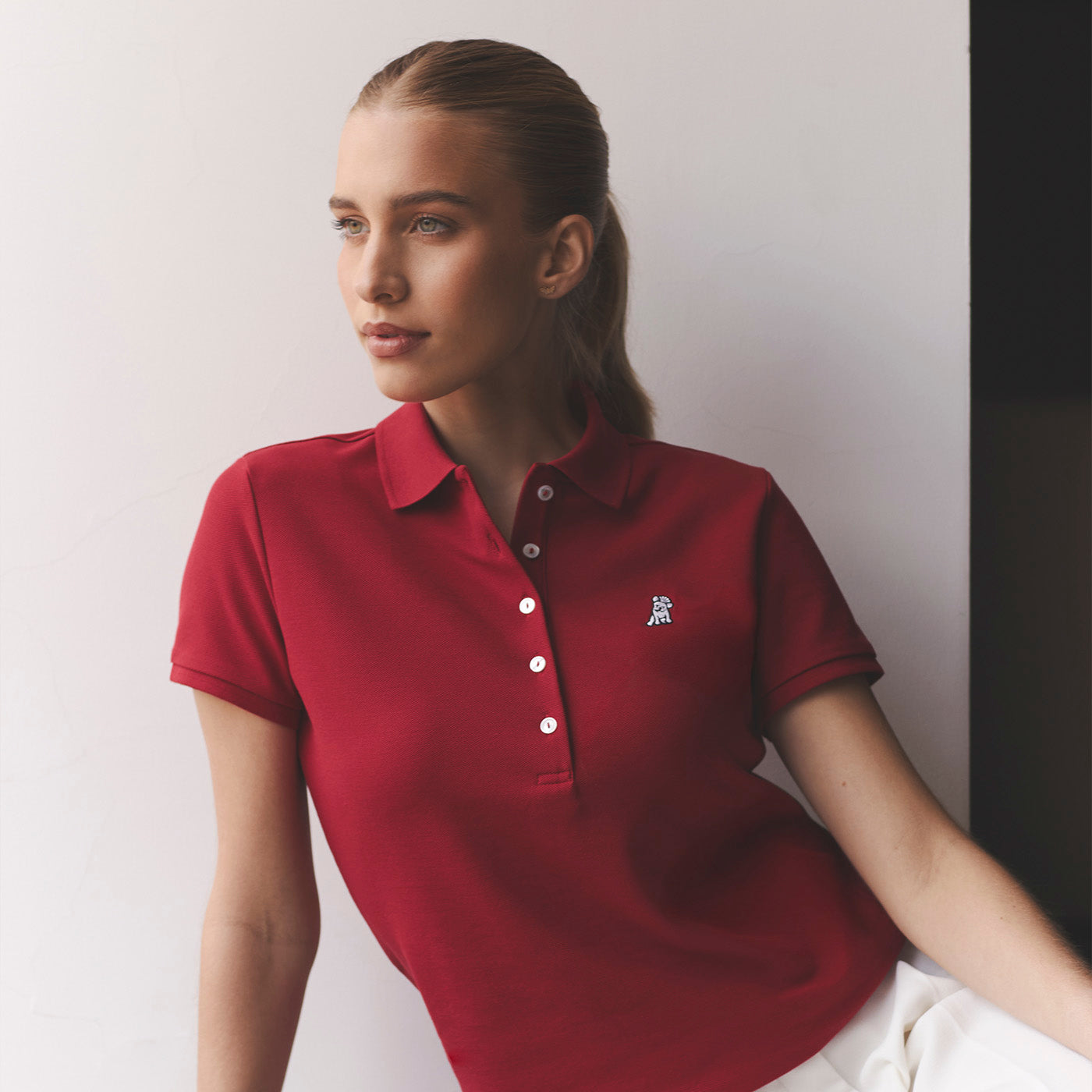 Woman wearing a red polo with a white dog logo on a grey background