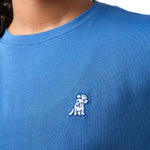 Close-up front view of a girl wearing the blue t-shirt with a small white embroidered logo on the chest.