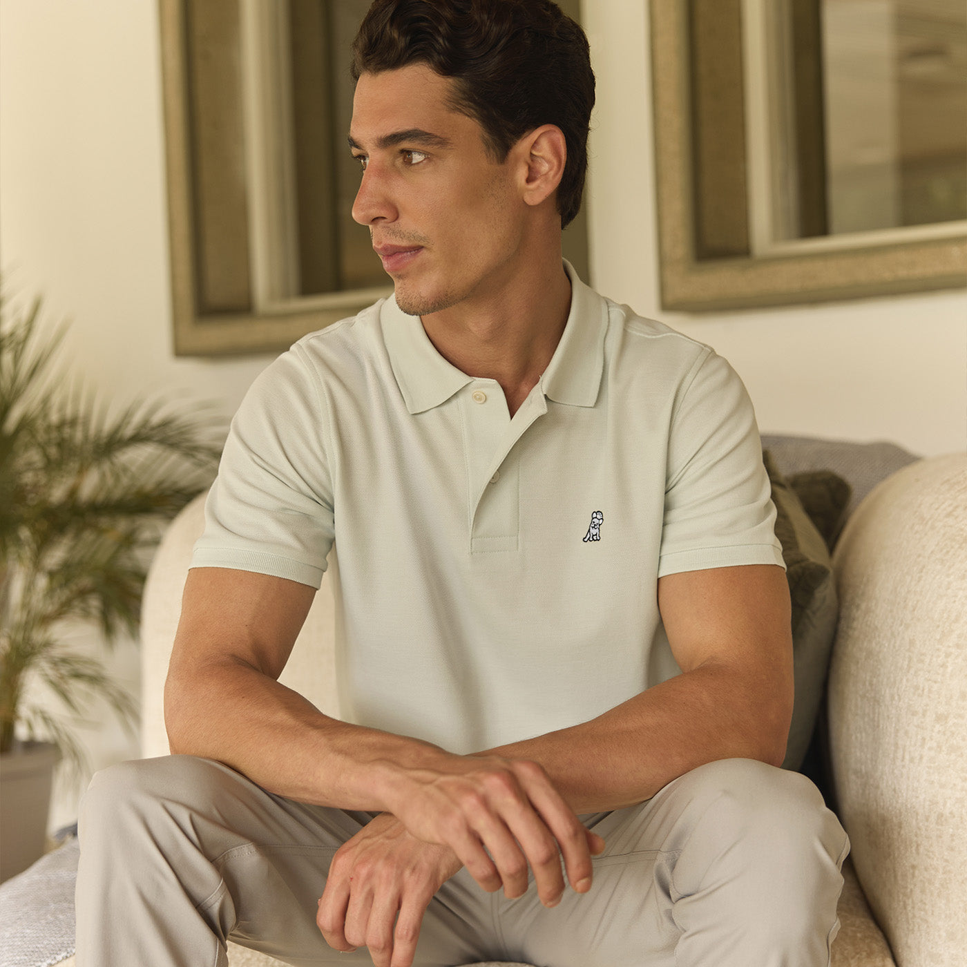 Man sitting on a couch wearing a light gray polo shirt with a small logo.