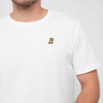 Close-up of a man wearing the white T-shirt, showing the small golden embroidered logo on the chest.