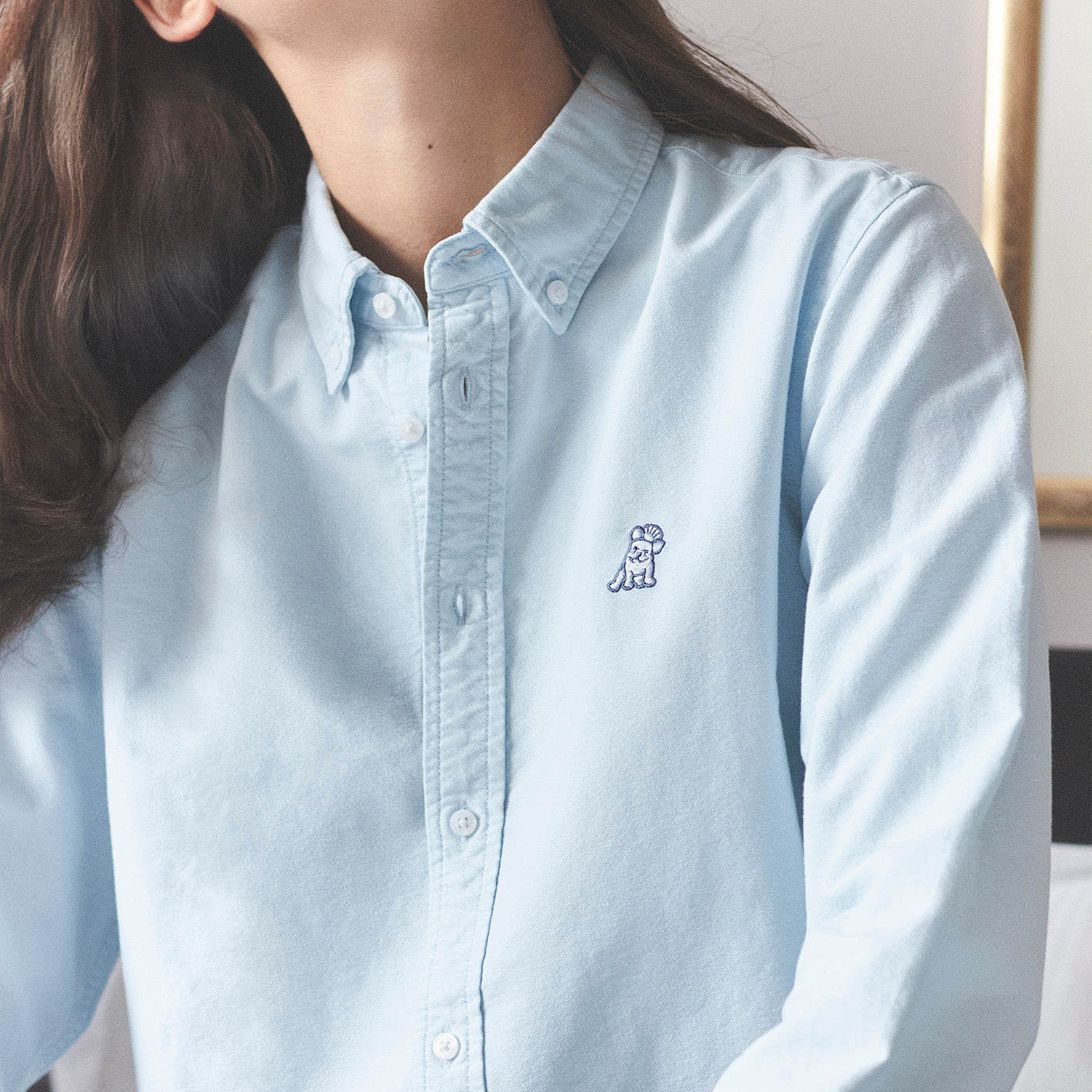 Light blue button-up shirt with a small logo worn by a person indoors.