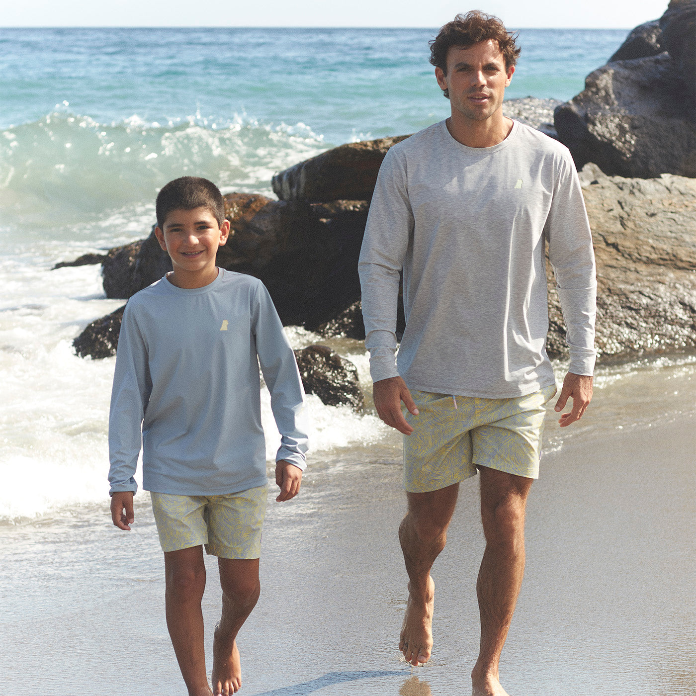 Man and boy walking on a beach with ocean waves in the background